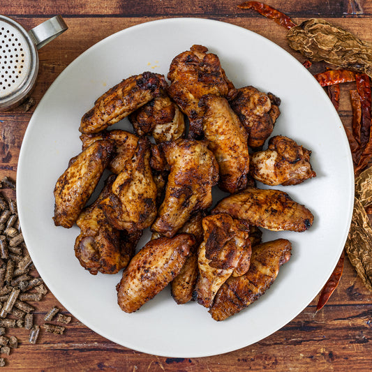 Platter of seasoned chicken wings on a wooden surface with spices.