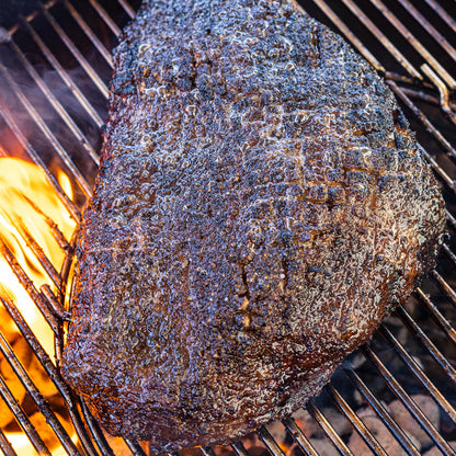 Seasoned steak with dark peppery bark cooking over fire on a charcoal grill