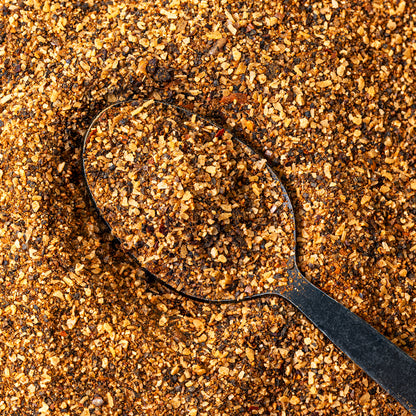 Macro close-up of Chiles and Smoke Canyon Crust Beef Seasoning, a coarse salt and pepper rub, on a black spoon