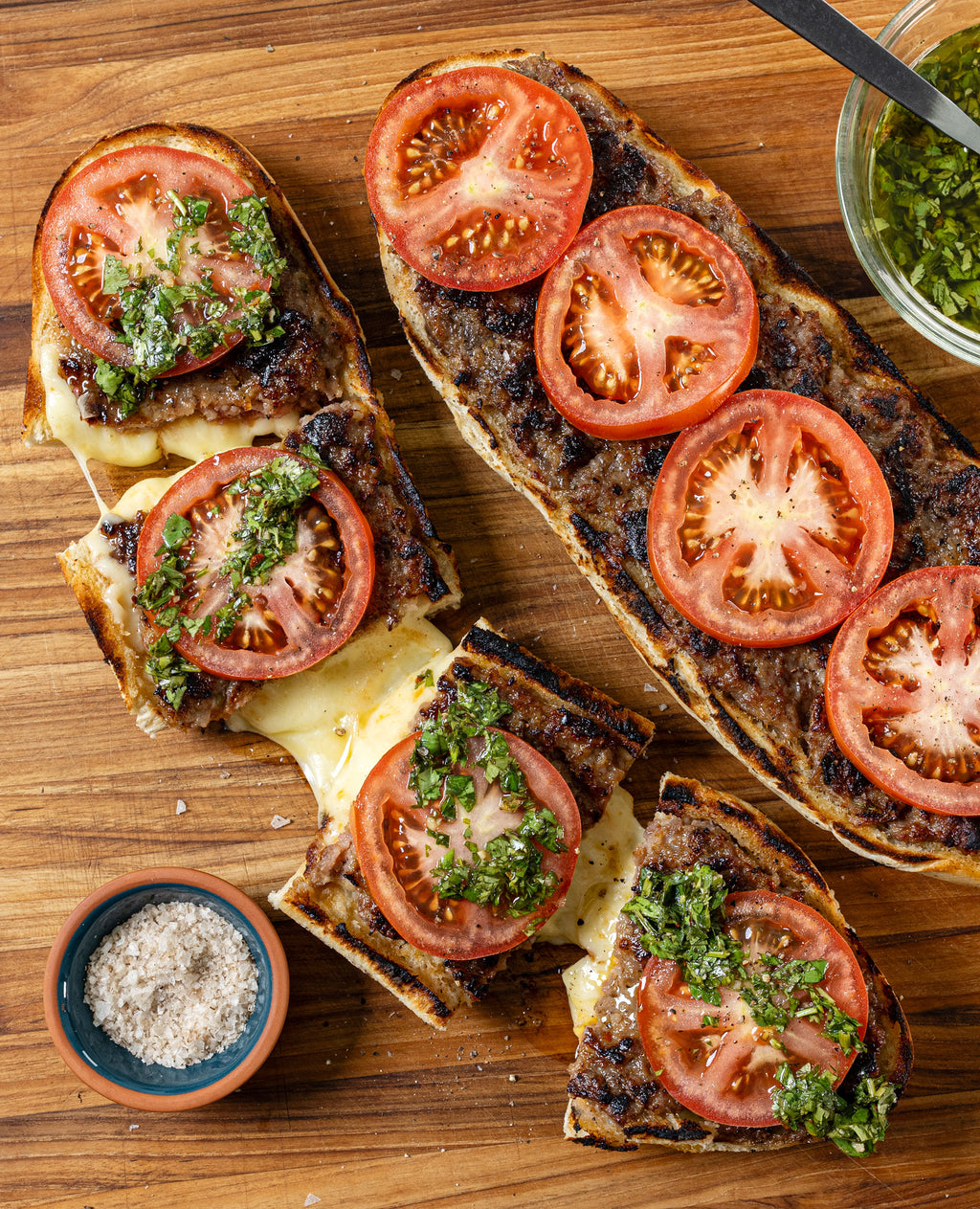 Grilled Choripan with Cheese and Chimichurri on a wooden cutting board