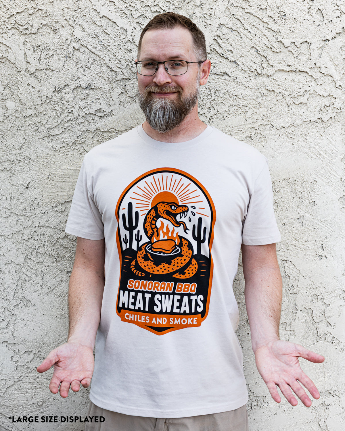 Brad Prose wearing a white t-shirt with a graphic design against a textured wall.