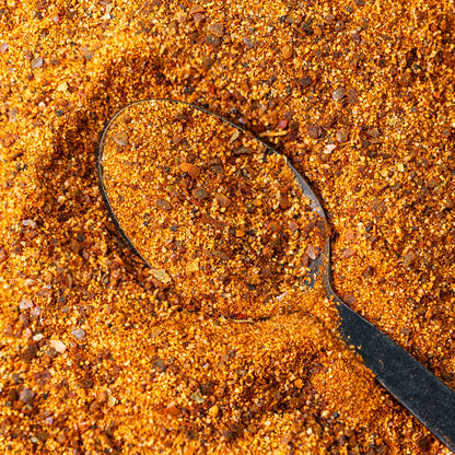 Macro close-up of Chiles and Smoke Scorching Sun Sweet Heat Rub on a black spoon, with chile flakes and sugar