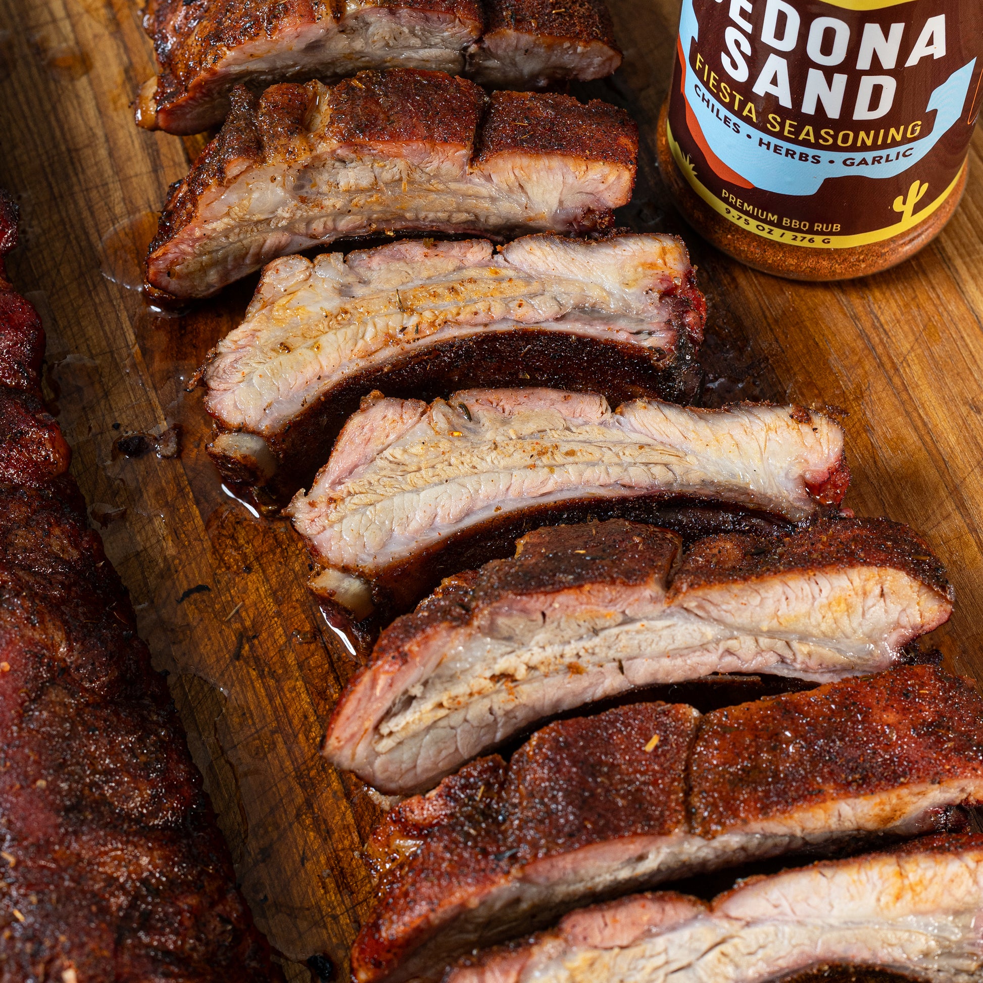 Smoked pork ribs sliced on a wood board next to Chiles and Smoke Sedona Sand seasoning
