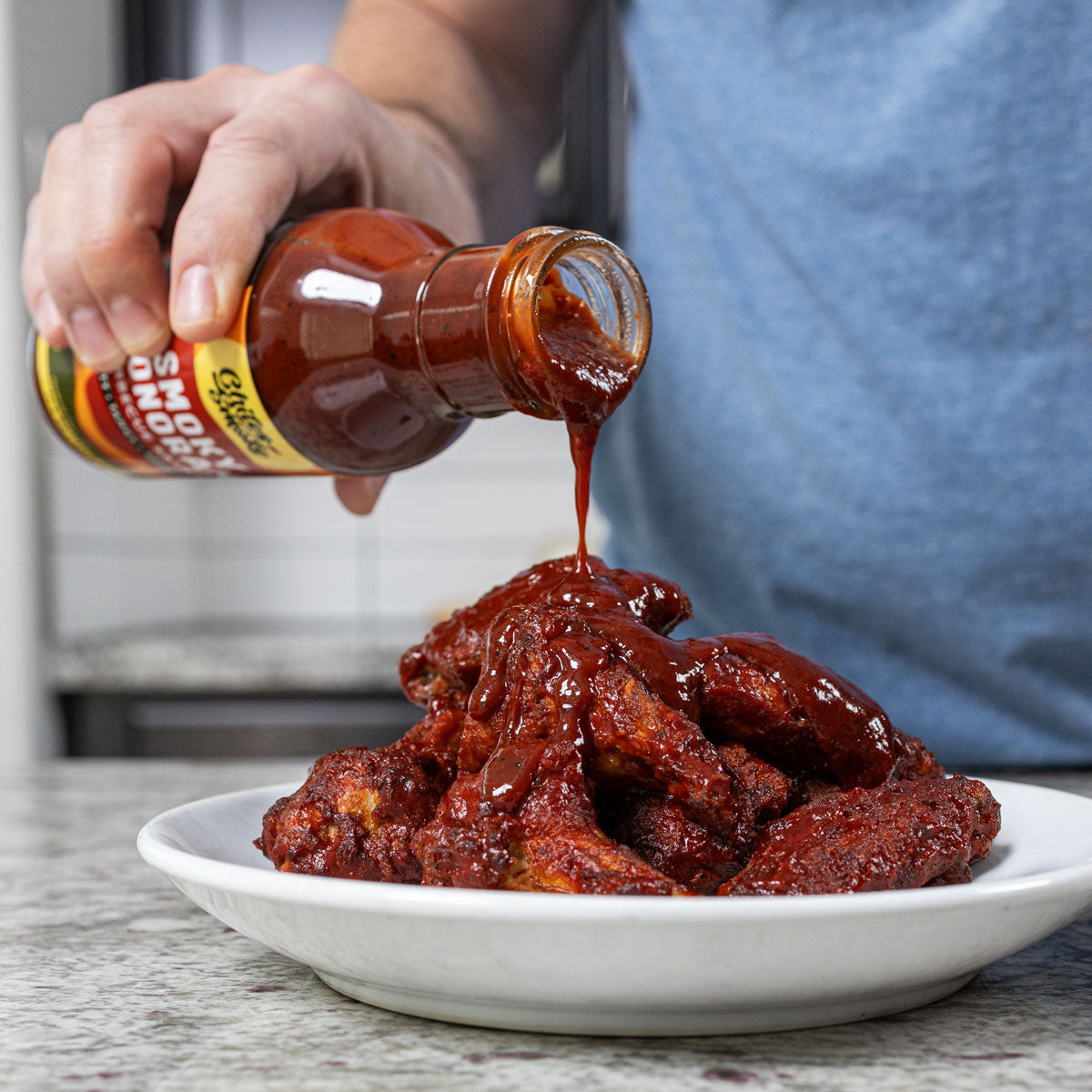 Pouring Chiles and Smoke Smoky Sonoran Barbecue Sauce over a plate of chicken wings